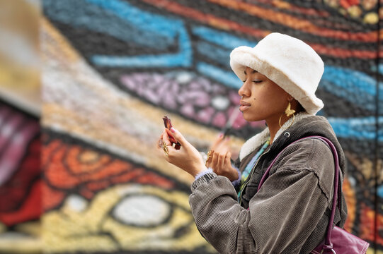 Side view of young woman looking at hand mirror against mural wall