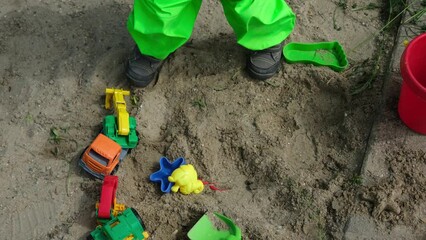 plastic toys on the sand, a boy in green pants