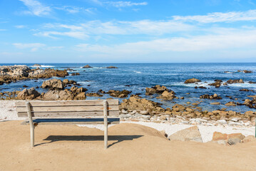 Fototapeta na wymiar Empty wooden bench facing a rocky beach and the ocean on a sunny fall day