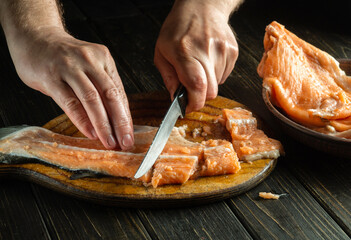 Slicing fresh fish on a kitchen cutting board before salting. Chef hands with a knife while cleaning pink salmon. The idea of a fish diet
