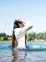 A young girl in a white shirt stands in the water splashing water