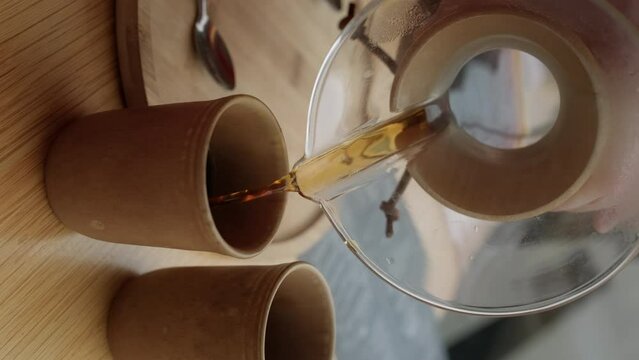 9x16 vertical video. Selective focus. Cozy morning atmosphere hand pouring freshly brewed batch brew coffee into clay mug in cafe.  Pouring steaming drip coffee with smoke ceramic cup 