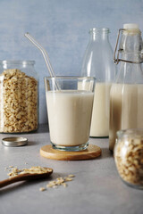 Oat milk in glass bottles with flakes on grey background. Protein healthy foods.
