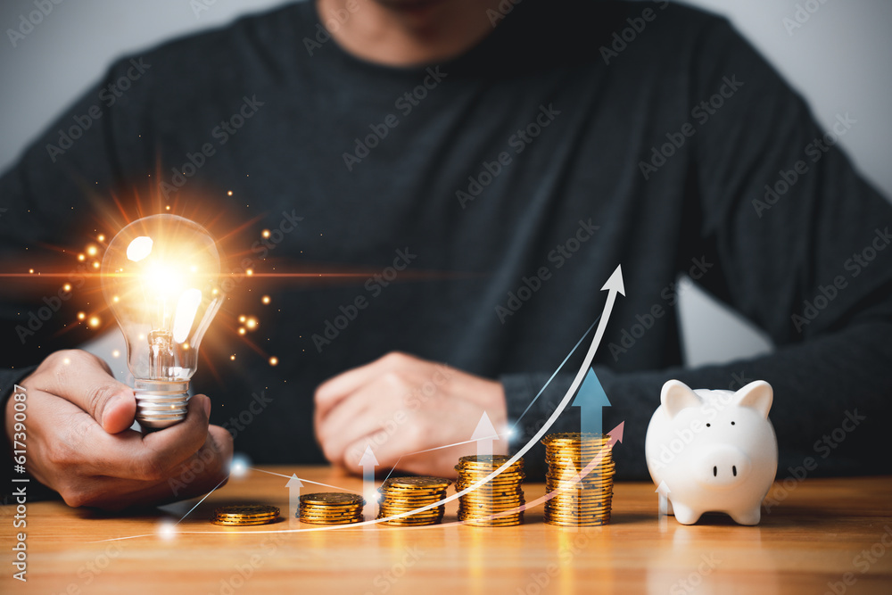 Poster hand holding a light bulb with coins stack and chart graph, representing creative concept of saving 