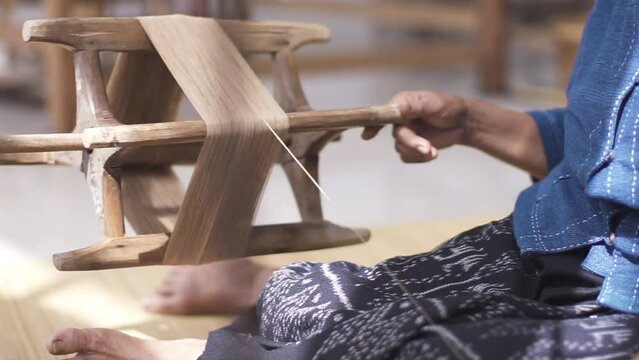 An elderly Asian woman is using a traditional spinning wheel made of wood.