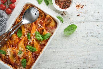 Cannelloni or conchiglioni. Baked stuffed pasta shells with bolognese meat sauce, tomatoes, basil on rustic white wooden table. Traditional Italian bolognese baked pasta with parmesan. Italian cuisine