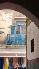 Fototapeta na wymiar Souvenir shop and part of a blue balcony with peeling paint seen through an arch over the road in the Medina in Essaouira, Morocco