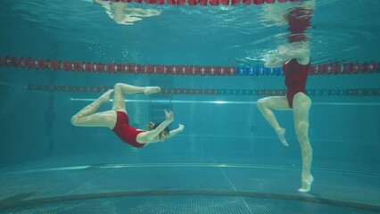 Professional swimmers in the pool, young womans perform the elements of synchronized swimming, beautiful dance under water.