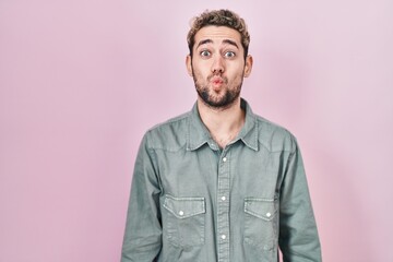 Hispanic man with beard standing over pink background making fish face with lips, crazy and comical gesture. funny expression.
