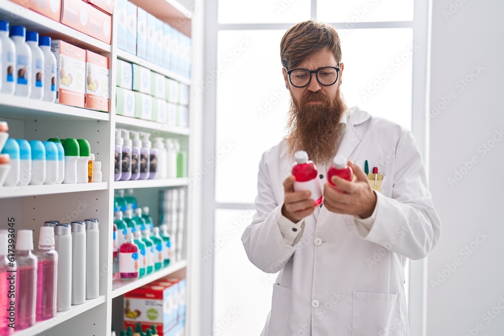 Wall mural young redhead man pharmacist holding medication bottle at pharmacy