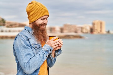 Young redhead man smiling confident drinking cup of coffee at seaside