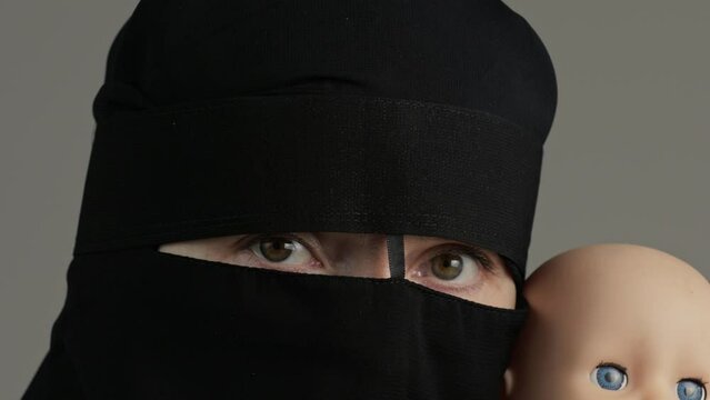 Muslim woman in black niqab with newborn doll