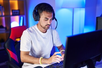 Young hispanic man streamer playing video game using computer at gaming room