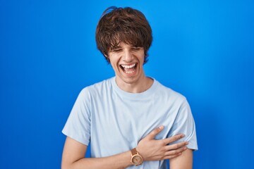 Hispanic young man standing over blue background smiling and laughing hard out loud because funny...