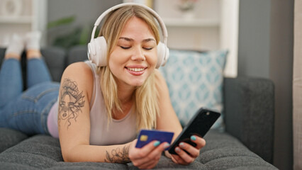 Young blonde woman shopping with smartphone and credit card listening to music at home