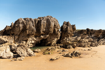 Fototapeta na wymiar Panoramic view of a cave formed on the beach by large rocks with a small lake of fresh sea water and golden sand on the coast of Asturias on a sunny day.