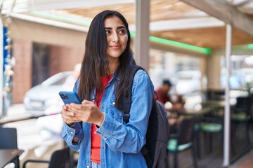 Young hispanic girl student smiling confident using smartphone at street