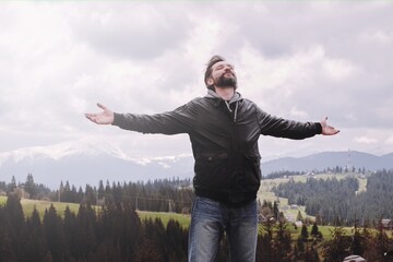 caucasian man on the background of Carpathian mountains. He spread his arms and closed his eyes. Wellness concept.