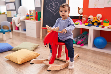Adorable hispanic boy playing with reindeer rocking at kindergarten