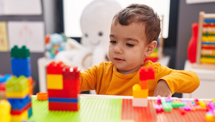 Adorable hispanic boy playing with construction blocks sitting on table at kindergarten