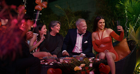 Indian Asian happy group friend young adult woman teen girl use mobile phone take selfie cam video old aged elder older male female boy man lady siting enjoy fun joy night dinner party outdoor home