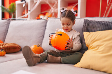 Adorable hispanic girl having halloween party holding pumpkin basket at home