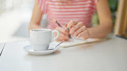 Young blonde woman sitting on table writing on notebook at coffee shop terrace