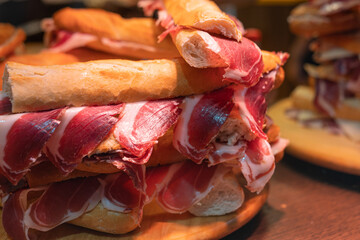 Spanish street food close-up, fresh baked baguette bread with sliced iberian cured ham jamon, bocadillo