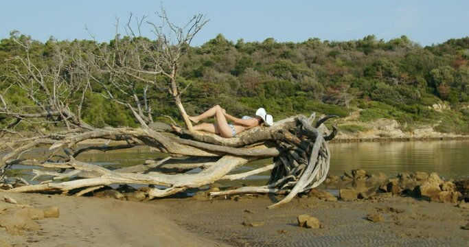 A young woman with a white hat is sitting on a sand beach, Rab Island, Croatia   
