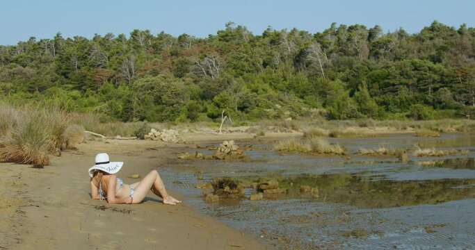 A young woman with a white hat is sitting on a sand beach, Rab Island, Croatia   