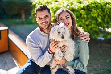 Man and woman holding dog hugging each other at park