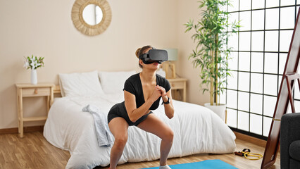 Young beautiful hispanic woman doing legs exercise using virtual reality glasses at bedroom