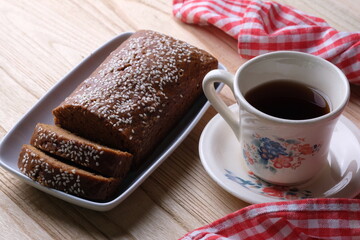 closeup of sesame-studded palm sugar bread slices on cooling rack. Indonesian traditional bread. Roti Ganjel Rel. a cup of coffee. 