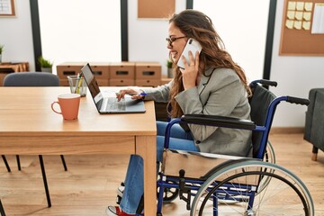 Young beautiful hispanic woman business worker talking on smartphone sitting on wheelchair at office