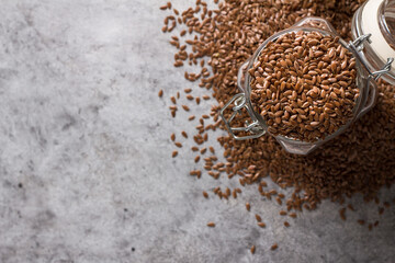 Flax seeds in a glass jar on a gray textured background, top view. Healthy food, superfood