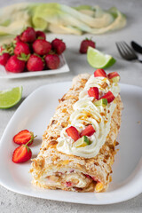 Meringue roll with strawberries and lime on light gray background, Vertical image
