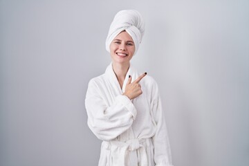 Blonde caucasian woman wearing bathrobe cheerful with a smile on face pointing with hand and finger up to the side with happy and natural expression