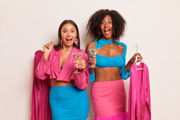 Two young women dressed in pink and blue clothes posing on white studio background, both girls hold...