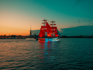 Sailing ship with red sails sailing on a surreal blue landscape with a rainbow. Artwork.