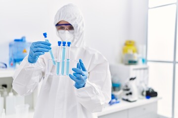 Young blonde woman scientist wearing security uniform holding test tubes at laboratory