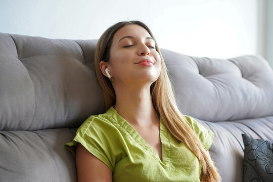 Pleased Girl In Earphones Listening To Music While Relaxing On Couch At Home