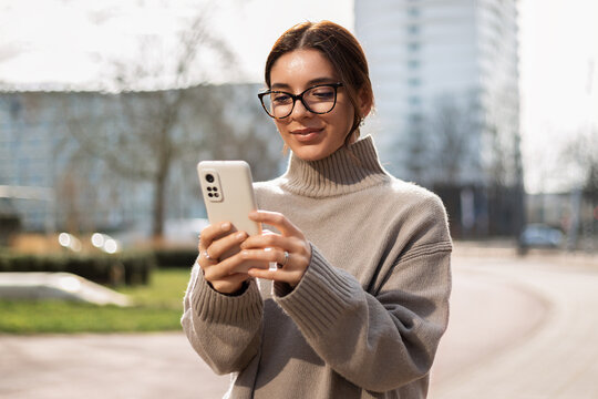 Beautiful woman student in eyeglasses using a phone in the street. Safe and happy