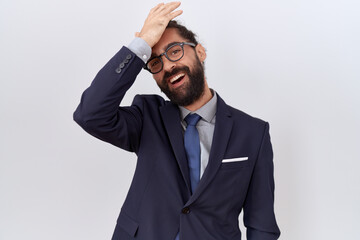 Hispanic man with beard wearing suit and tie surprised with hand on head for mistake, remember error. forgot, bad memory concept.