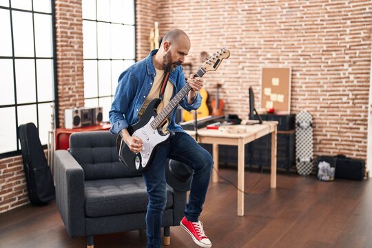 Young bald man musician playing electrical guitar standing at music studio