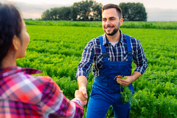 The Caucasian farmer and the Chinese agronomist in a carrot field have closed a deal. They shake hands, satisfied with the yields and their successful collaboration.