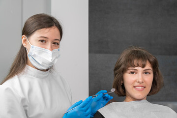 Young smiling woman is sitting in a dental chair, a dentist is sitting next to them, they are...