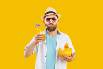 Portrait of a funny bearded man in beach hat and sunglasses drinking orange juice cocktail holding...