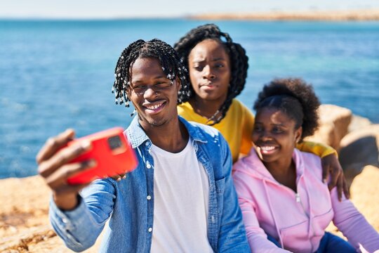 African american friends making selfie by the smartphone sitting on rock at seaside