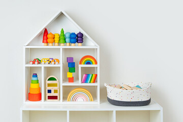 White house shaped shelving with colorful wooden toys on white wall. Interior design. Organizing and Storage Ideas in nursery.