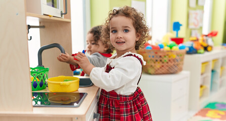 Adorable girls playing with play kitchen standing at kindergarten